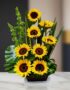 Arreglo floral premium con girasoles Bengala, hojas verdes y follaje, sobre una mesa de mármol en un lobby de hotel boutique.