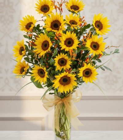 Arreglo floral de girasoles LENU en un jarrón de cristal con lazo dorado, sobre una mesa de mármol y fondo elegante.