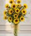 Arreglo floral de girasoles LENU en un jarrón de cristal con lazo dorado, sobre una mesa de mármol y fondo elegante.