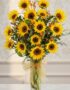 Arreglo floral de girasoles LENU en un jarrón de cristal con lazo dorado, sobre una mesa de mármol y fondo elegante.
