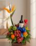 Arreglo floral gourmet ITALINA con ave del paraíso, vino tinto, uvas, manzanas, naranjas y ciruelas, sobre una mesa de madera