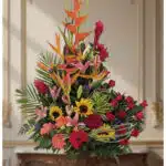 Arreglo floral IDARA con rosas rojas, girasoles, lirios, heliconias y jengibre rojo en un fondo elegante y bien iluminado.