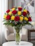 Arreglo floral LORENZA con 24 rosas rojas y amarillas en un jarrón de cristal, sobre una mesa blanca con fondo elegante y luz