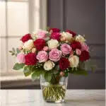 Arreglo floral LUCREZIA con 30 rosas en tonos románticos (rojas, rosas y blancas) en un jarrón de cristal, sobre una mesa de
