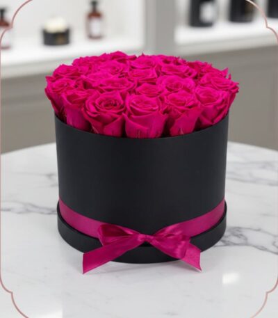 Arreglo Floral Marena con 21 rosas fucsia vibrantes y frescas en una caja redonda negra con lazo fucsia, sobre una mesa de má