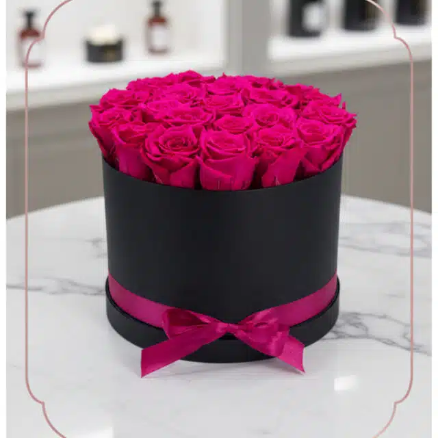 Arreglo Floral Marena con 21 rosas fucsia vibrantes y frescas en una caja redonda negra con lazo fucsia, sobre una mesa de má