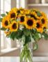 Arreglo floral MARTINA con 21 girasoles vibrantes y hojas de eucalipto en un jarrón de cristal, sobre una mesa de mármol con