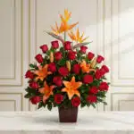 Arreglo floral 'Me Encantas' con lirios naranjas, rosas rojas y aves del paraíso, sobre una mesa de mármol en un entorno eleg