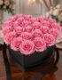 Arreglo Floral Perla con 24 rosas rosadas vibrantes en una caja negra en forma de corazón, sobre una mesa de madera pulida en