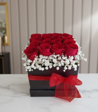 Arreglo floral Pétalos con rosas rojas frescas y gypsophila en una caja negra con lazo rojo, sobre mármol blanco en un entorn