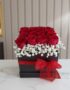 Arreglo floral Pétalos con rosas rojas frescas y gypsophila en una caja negra con lazo rojo, sobre mármol blanco en un entorn
