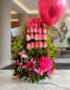 Arreglo floral premium 'Quiero que Sepas' con rosas rosadas, lirios, follaje verde y un globo fucsia, sobre mármol en un lobb