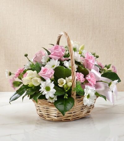 Cesta de mimbre con 12 rosas rosadas, margaritas blancas, freesias y claveles, ideal para regalar en ocasiones especiales.