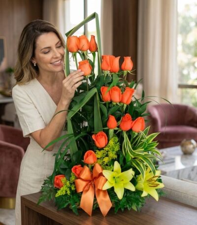 Mujer elegante de mediana edad admirando con deleite un arreglo floral Romeo con rosas naranjas, lirios amarillos y follaje v