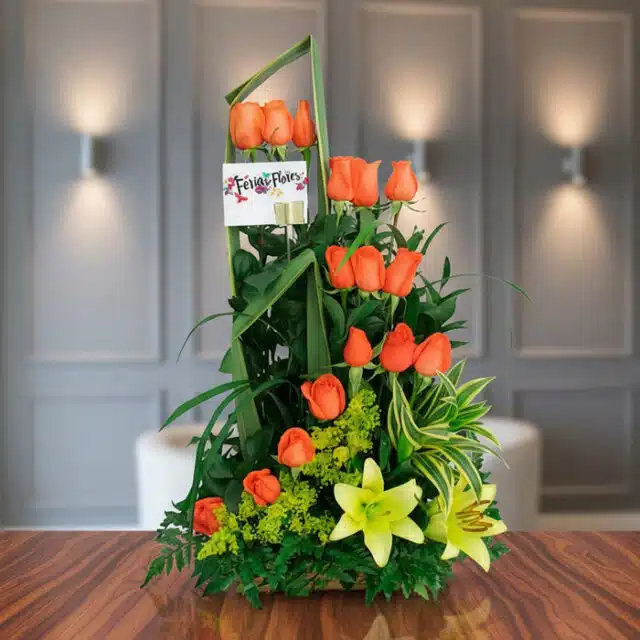 Arreglo floral Romeo con rosas naranjas vibrantes y lirios amarillos, sobre una superficie de madera pulida en un entorno ele