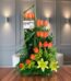 Arreglo floral Romeo con rosas naranjas vibrantes y lirios amarillos, sobre una superficie de madera pulida en un entorno ele