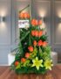 Arreglo floral Romeo con rosas naranjas vibrantes y lirios amarillos, sobre una superficie de madera pulida en un entorno ele
