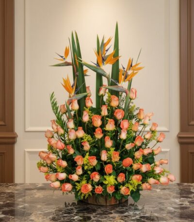 Arreglo floral grande con rosas color salmón y aves del paraíso, sobre una mesa de mármol en un entorno elegante de hotel bou