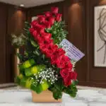 Arreglo floral premium con rosas rojas en espiral, follaje verde y flores blancas, sobre mármol en un entorno elegante.