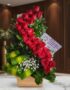 Arreglo floral premium con rosas rojas en espiral, follaje verde y flores blancas, sobre mármol en un entorno elegante.