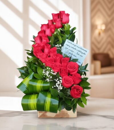 Arreglo floral premium con rosas rojas voluta, follaje verde y detalles blancos, sobre una superficie de mármol en un entorno