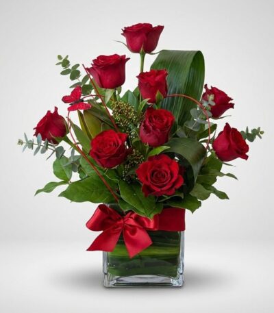 Arreglo floral ROSETTA con seis rosas rojas frescas, follaje verde y un lazo rojo en un jarrón de cristal, ideal para regalar