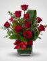 Arreglo floral ROSETTA con seis rosas rojas frescas, follaje verde y un lazo rojo en un jarrón de cristal, ideal para regalar