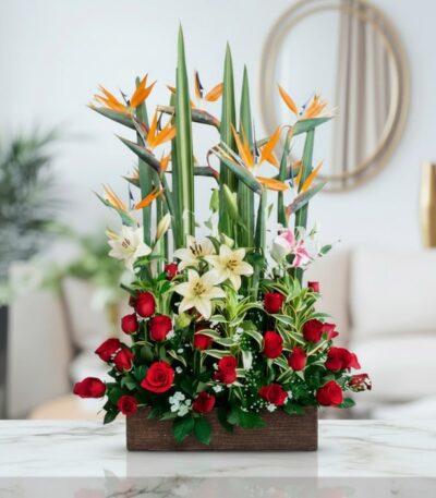 Arreglo floral 'Siempre Juntos' con aves del paraíso, lirios blancos y rosas rojas en base de madera, sobre mármol.