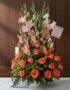 Arreglo floral Suspiro con gladiolos rosados y blancos, rosas naranjas y lirios, sobre una superficie de mármol en un entorno