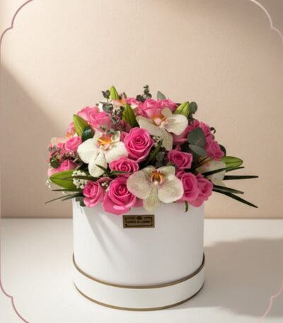 Arreglo floral TANIA con rosas rosadas vibrantes y orquídeas blancas delicadas en una caja redonda blanca con borde dorado, i