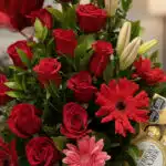 Primer plano extremo de un arreglo floral 'Te Amo' con rosas rojas vibrantes, lirios blancos y gerberas, mostrando texturas h