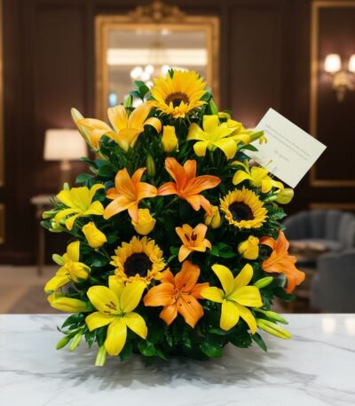 Arreglo floral tropical vibrante con girasoles, lirios amarillos y naranjas, y follaje verde, sobre una superficie de mármol
