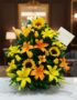 Arreglo floral tropical vibrante con girasoles, lirios amarillos y naranjas, y follaje verde, sobre una superficie de mármol