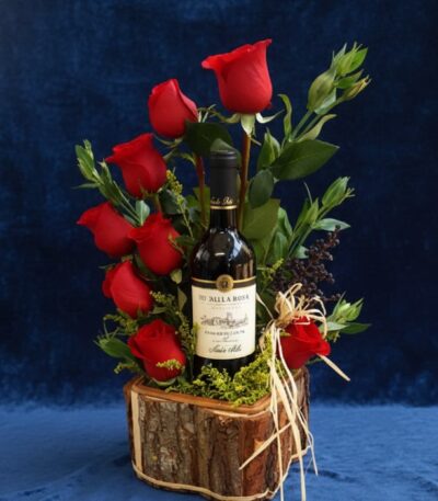 Arreglo floral VERITA con rosas rojas frescas y una botella de vino tinto, presentado en una base de madera rústica, ideal pa