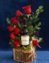 Arreglo floral VERITA con rosas rojas frescas y una botella de vino tinto, presentado en una base de madera rústica, ideal pa