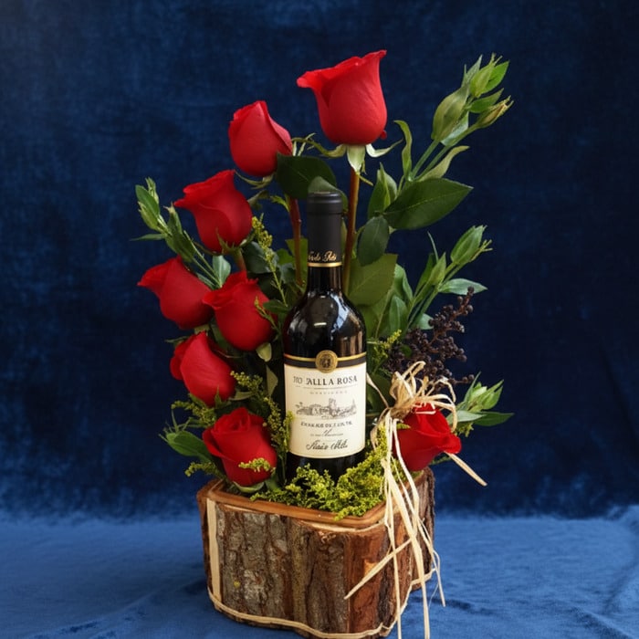 Arreglo floral VERITA con rosas rojas frescas y una botella de vino tinto, presentado en una base de madera rústica, ideal pa
