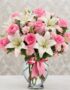 Arreglo floral vibrante con rosas rosadas, lirios blancos y claveles rosados en un jarrón de cristal con lazo rosa, ideal par