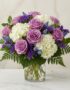 Arreglo floral VITTORIA con rosas lilas, hortensias blancas y muscari azul en un jarrón de cristal, sobre una mesa de mármol.