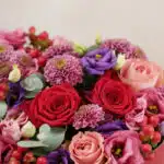 Primer plano extremo del Arreglo Floral ZITA, mostrando rosas rojas y rosadas, lisianthus morados, crisantemos púrpuras y bay