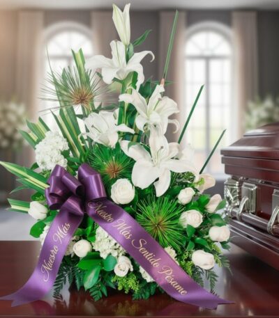 Arreglo floral fúnebre 'Adiós Para Siempre' con lirios blancos, rosas y follaje verde, adornado con cinta morada 'Nuestro Más