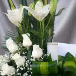 Fotografía macro premium de Arreglo Fúnebre Claridad con lirios y rosas blancas, rocío sutil, cinta satinada y follaje verde.