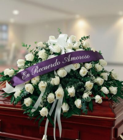 Arreglo fúnebre cubre caja Misericordia con rosas blancas y follaje verde, adornado con una cinta morada que dice 'En Recuerd