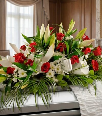 Arreglo fúnebre cubre caja Paraíso con rosas rojas, lirios blancos y margaritas, sobre un ataúd en una sala de velación premi