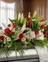 Arreglo fúnebre cubre caja Paraíso con rosas rojas, lirios blancos y margaritas, sobre un ataúd en una sala de velación premi
