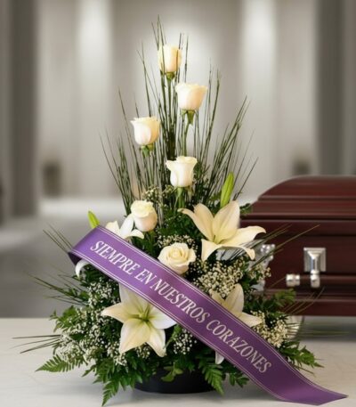 Arreglo fúnebre 'Descanso Eterno' con rosas blancas, lirios y follaje, adornado con una cinta morada que dice 'SIEMPRE EN NUE