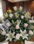 Arreglo fúnebre Infinito con lirios blancos y rosas pálidas, presentado en una sala de velación premium con luz natural suave