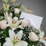 Fotografía macro premium del Arreglo Fúnebre Infinito con lirios blancos, rosas pálidas y follaje verde, con rocío sutil y ci