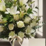 Fotografía macro premium de Arreglo Fúnebre Perpetuo con lirios y rosas blancas, follaje verde, rocío sutil y cinta satinada.
