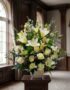 Arreglo fúnebre perpetuo con lirios blancos, rosas blancas y follaje verde, presentado en una sala de velación premium con lu