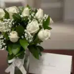 Fotografía macro premium del Arreglo Fúnebre Pétalos del Alma con rosas blancas, follaje verde, rocío sutil y cinta satinada.